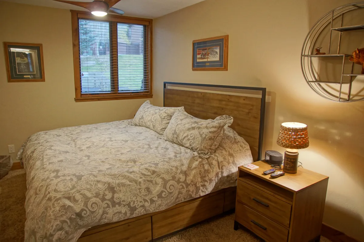 A serene bedroom with a neatly made bed, soft lighting from a bedside lamp, a nightstand, and a large window letting in natural light. The room exudes a calm and inviting atmosphere, perfect for unwinding after an active day.