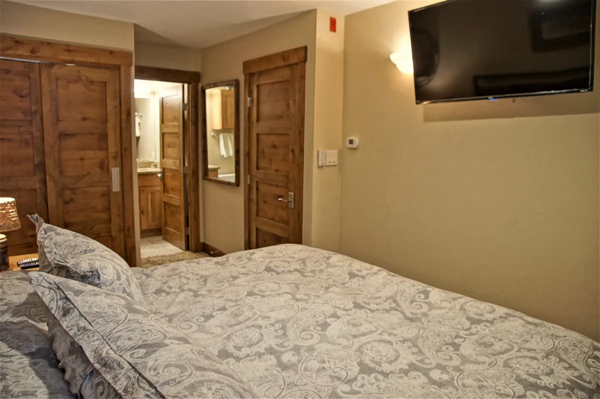 A comfortable bedroom with a patterned bedspread, wooden doors, a wall-mounted TV, and thoughtful decor. The space feels private and cozy, ideal for evenings spent relaxing or enjoying a quiet movie night.