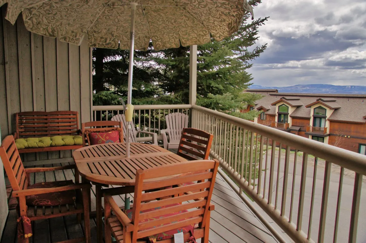 A welcoming outdoor dining area with a wooden table under an umbrella, surrounded by trees and lounge chairs. The setup invites guests to dine alfresco, sip morning coffee, or gather for evening conversations, with the surrounding landscape promising year-round enjoyment.