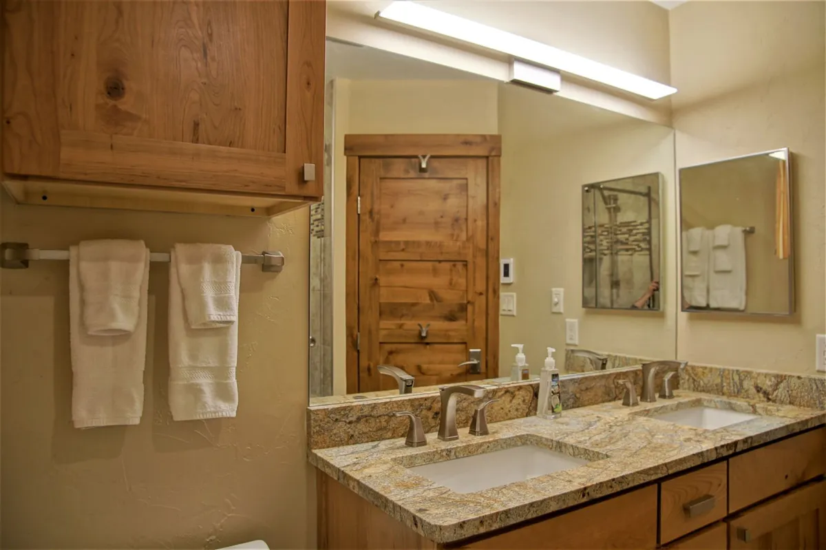 A modern bathroom featuring granite countertops, double sinks, and wooden cabinetry. The mirrored surfaces and ample counter space suggest convenience and comfort for families or larger groups preparing for special occasions or starting the day together.