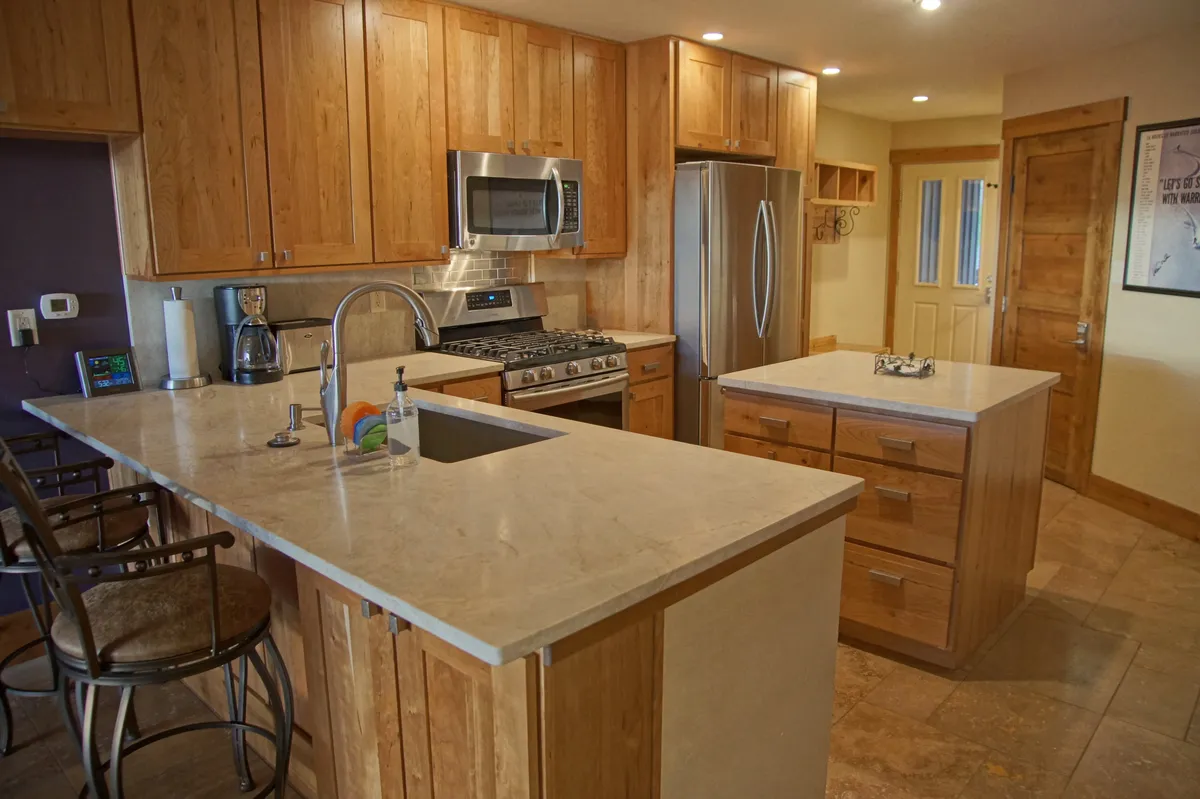 A modern kitchen with a spacious island, stainless steel appliances, and wood cabinetry, all designed for convenience and efficiency. The open layout is well-lit and inviting, suggesting ease of meal preparation and social interaction.