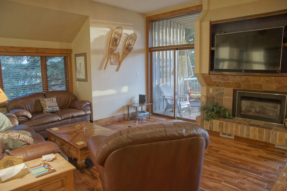 A spacious living area featuring comfortable leather sofas arranged around a stone fireplace, with large windows letting in natural light and views of the outdoors. Decorative touches such as snowshoes on the wall create a cozy, mountain-lodge atmosphere, ideal for relaxation and socializing.