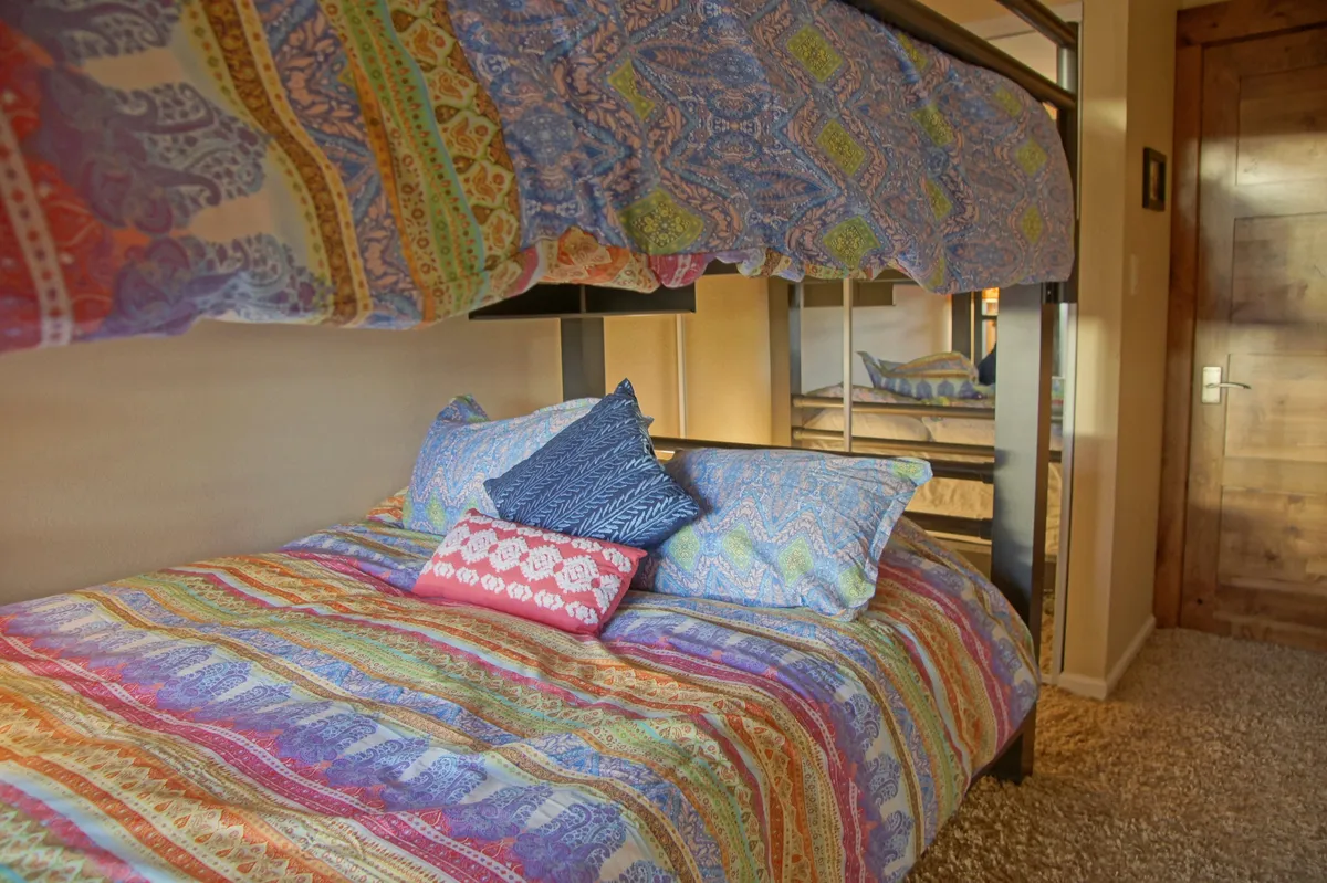 A cheerful bedroom with a bunk bed adorned in colorful bedding and decorative pillows. The playful yet inviting space is well-suited for children, families, or groups seeking flexible sleeping arrangements.