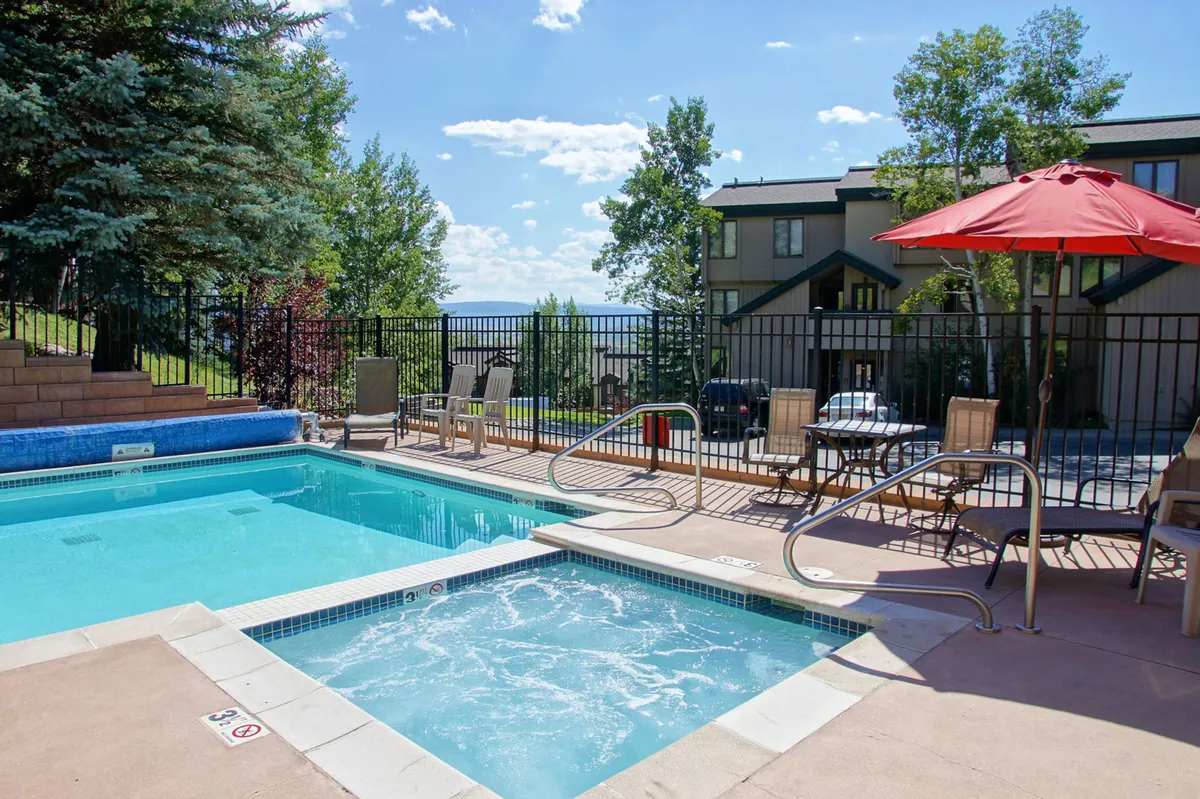 This image features a sparkling swimming pool and adjacent hot tub, surrounded by lounge chairs and a vibrant red umbrella. The scene is set outdoors, inviting guests to relax, swim, or sunbathe, with a clear view of the tranquil resort atmosphere.