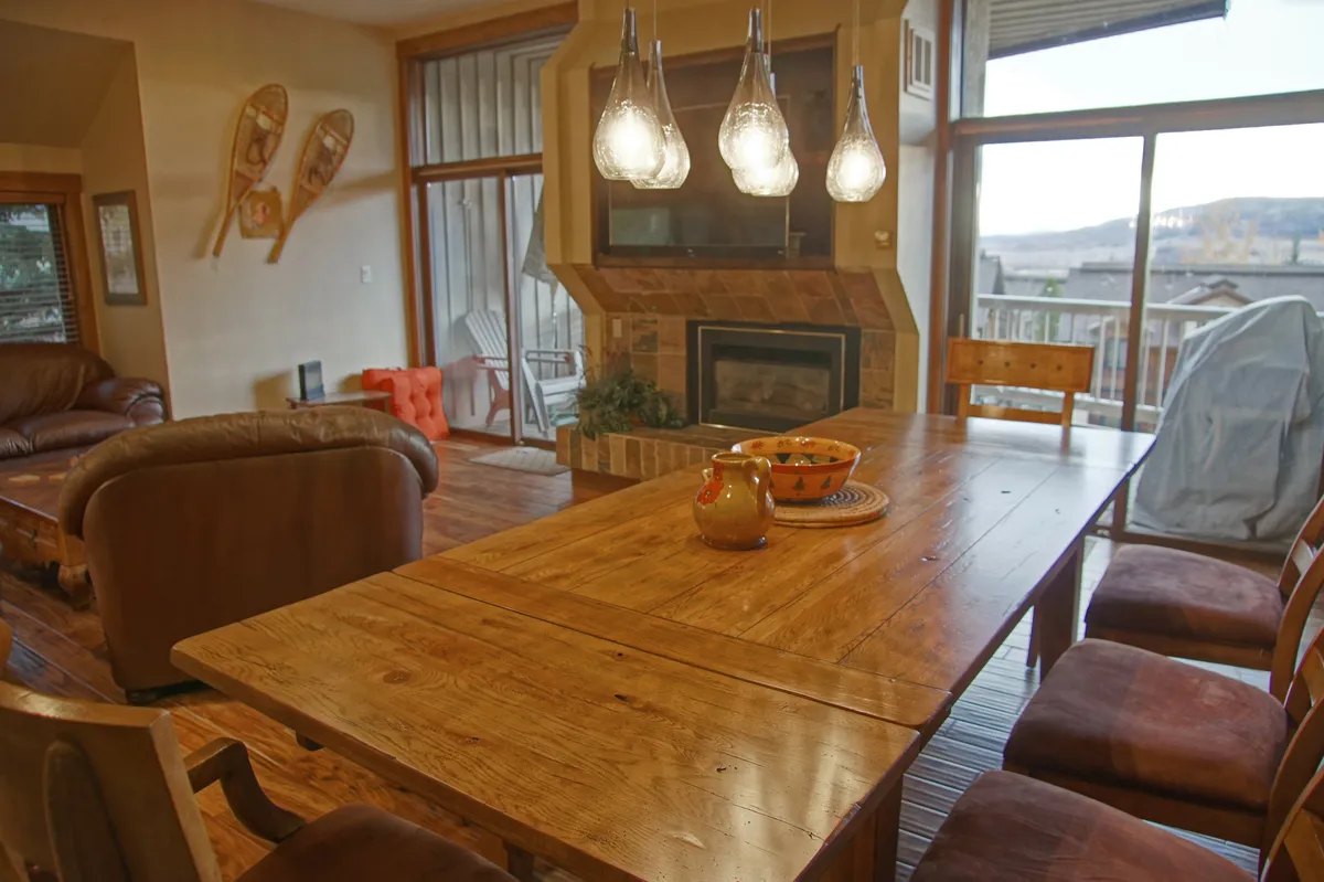 A bright dining space with a sturdy table under modern pendant lights, adjacent to a cozy fireplace and large window offering valley views. The setup invites gatherings, intimate meals, and peaceful mornings with coffee.